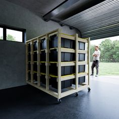 a man standing next to a tall wooden cart filled with black boxes in a garage