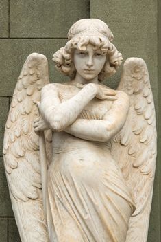 an angel statue is standing next to a brick wall with its arms crossed and hands folded