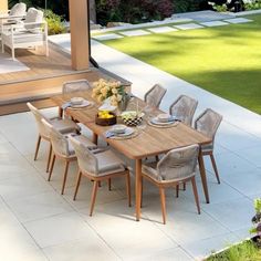 an outdoor dining table with six chairs and plates on it in the middle of a patio