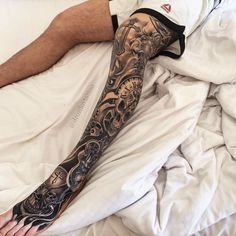 a man laying on top of a bed covered in white sheets with his arm and leg tattoos