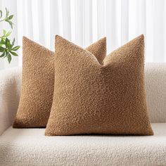 two brown pillows sitting on top of a white couch next to a potted plant