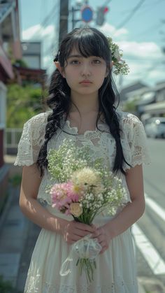 a girl in a white dress holding a bouquet of flowers on the side of the road