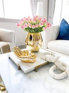 a living room with white couches and pink flowers in a vase on a tray