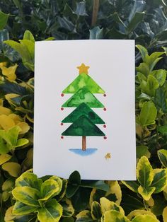 a card with a watercolor christmas tree on it in front of some green leaves