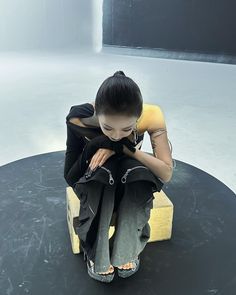 a woman sitting on top of a black table next to a yellow chair and looking down