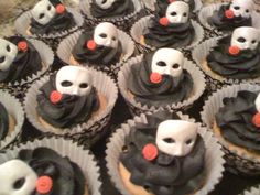 many cupcakes with black frosting and white masks on them are arranged in rows