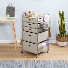 a metal cart with five drawers on wheels in front of a blue wall and potted plant