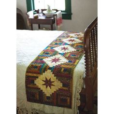 a bed with a quilt on top of it next to a chair and table in front of a window