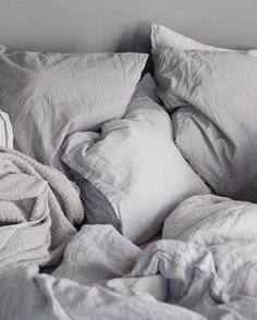 an unmade bed with white sheets and pillows