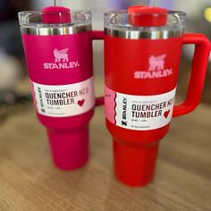 two red and pink coffee cups sitting on top of a wooden table next to each other