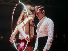 a man standing next to a woman holding a hoop in front of her face on top of a stage