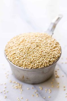 a metal bowl filled with sesame seeds on top of a white countertop next to a spoon