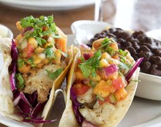 two fish tacos on a white plate with beans and salsa in the background,