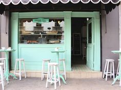 the outside of a bakery with pastel green paint and white stools in front of it