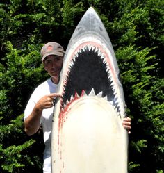 a man holding a surfboard with a shark's mouth painted on the side