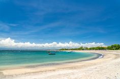 a beach with boats on the water and clouds in the blue sky above it,