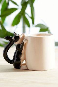 a black and white cat figurine sitting in front of a coffee cup on a table