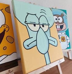 three cartoon paintings are displayed on easels