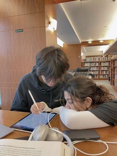 two people sitting at a table with an electronic device and book in front of them