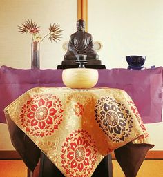 a buddha statue sitting on top of a wooden table next to a purple and gold cloth