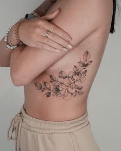 a woman's stomach with flowers and leaves tattooed on the side by her arm