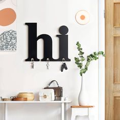 a white table topped with a metal letter mounted to the wall next to a vase filled with flowers