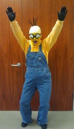 a man dressed as a minion with his hands in the air and wearing overalls