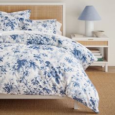 a bed with blue and white floral comforter on top of it in a bedroom