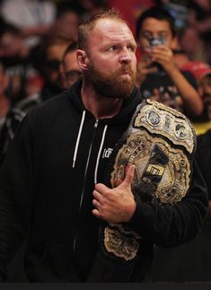 a man with a beard holding a wrestling belt in front of a group of people