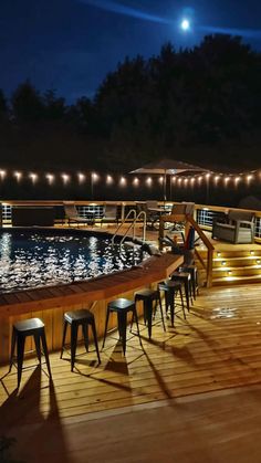 an outdoor deck with bar stools next to a swimming pool at night under lights