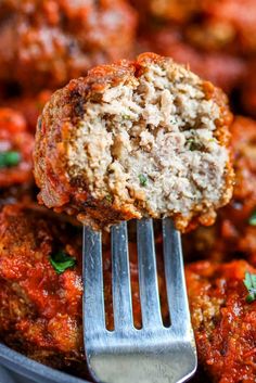 a close up of meatballs on a fork in a bowl with sauce and parsley