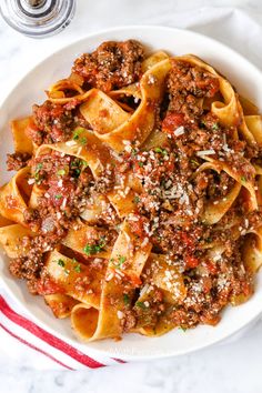 a white bowl filled with pasta covered in meat and sauce on top of a table