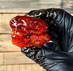 a person wearing black gloves holding up a piece of meat with ketchup on it