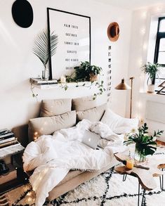 an unmade bed in a white room with plants on the headboard and lights hanging from the ceiling