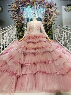 a pink dress on display in front of a white railing with flowers and chandelier