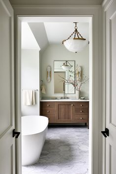 a bath room with a large white tub and a sink under a light hanging from a chandelier