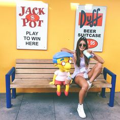 a woman sitting on a bench next to a simpsons stuffed animal drinking from a bottle