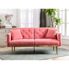 a pink couch sitting on top of a wooden floor next to a potted plant