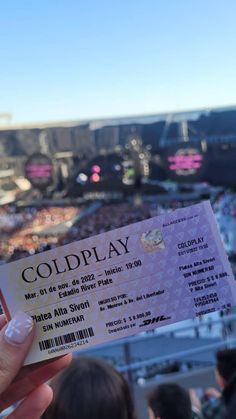 a person holding up a ticket for coldplay in front of a crowd at a concert