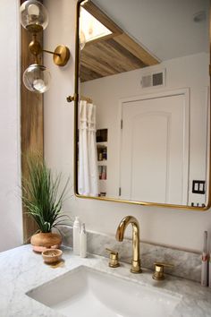 a bathroom sink with a large mirror and gold faucet on the wall above it