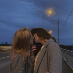 two women kissing each other while standing on the side of a road at night time