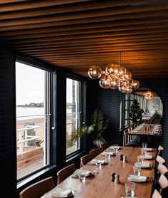 a long wooden table with white plates and place settings in front of large windows overlooking the water