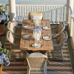 an outdoor dining table with wicker chairs and place settings on a deck overlooking the ocean