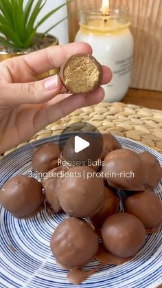 a person is holding up some chocolates on a blue and white plate with a candle in the background