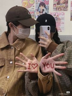 two people wearing face masks and holding up their hands with the words i love you written on them