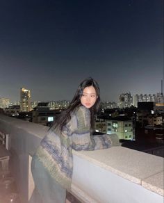 a woman standing on top of a balcony next to a tall building with buildings in the background