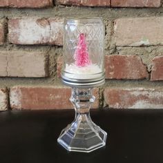 a small glass candle holder with a pink christmas tree in it on a table next to a brick wall