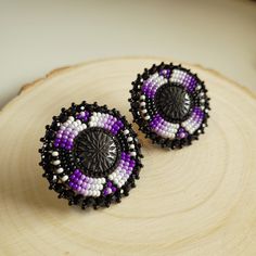 two purple and white beaded earrings sitting on top of a piece of wood