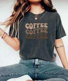 Start your day right with the Comfort Colors Coffee Shirt, a must-have for any coffee enthusiast! This Coffee Lover Tee features the fun slogan "But First, Coffee," perfect for showcasing your love for caffeine. Made from ultra-soft Comfort Colors fabric, this Coffee Addict TShirt ensures maximum comfort and durability. Available in oversized plus sizes, it provides a relaxed and flattering fit for everyone. Whether you're treating yourself or looking for the perfect gift for her, this Caffeine Coffee Colored Relaxed Fit T-shirt With Slogan, Casual Coffee Slogan T-shirt, Casual Coffee Colored Slogan T-shirt, Casual Coffee T-shirt With Slogan, Coffee Colored Relaxed Fit Tops With Graphic Print, Relaxed Fit Coffee Tops With Graphic Print, Casual Coffee Colored Everyday Tops, Casual Coffee Colored Top For Everyday, Everyday Coffee-colored Graphic Tee