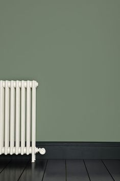 a white radiator sitting on top of a hard wood floor next to a green wall